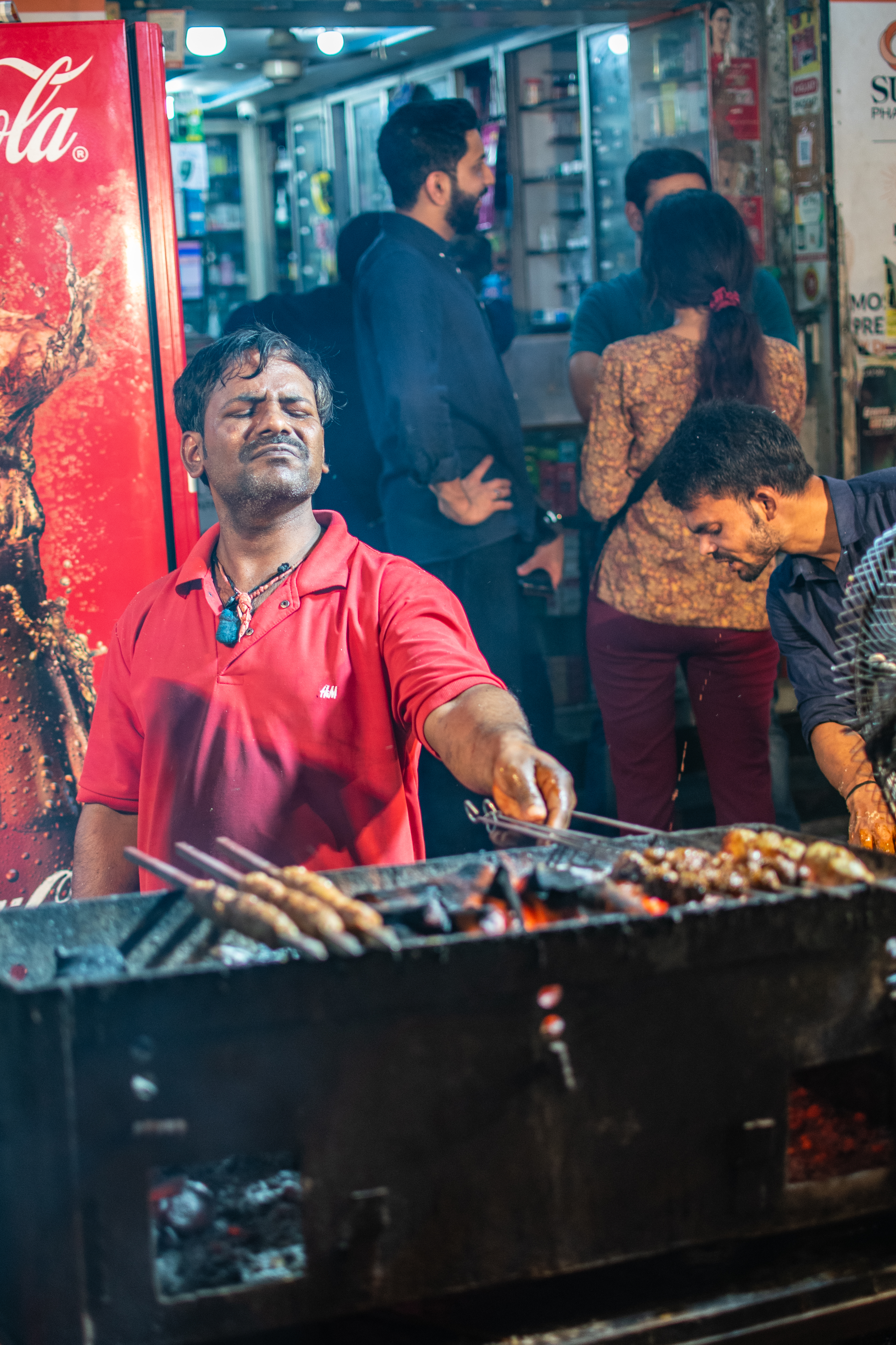 Vendor at the grill, eyes closed, arm reaching over fire