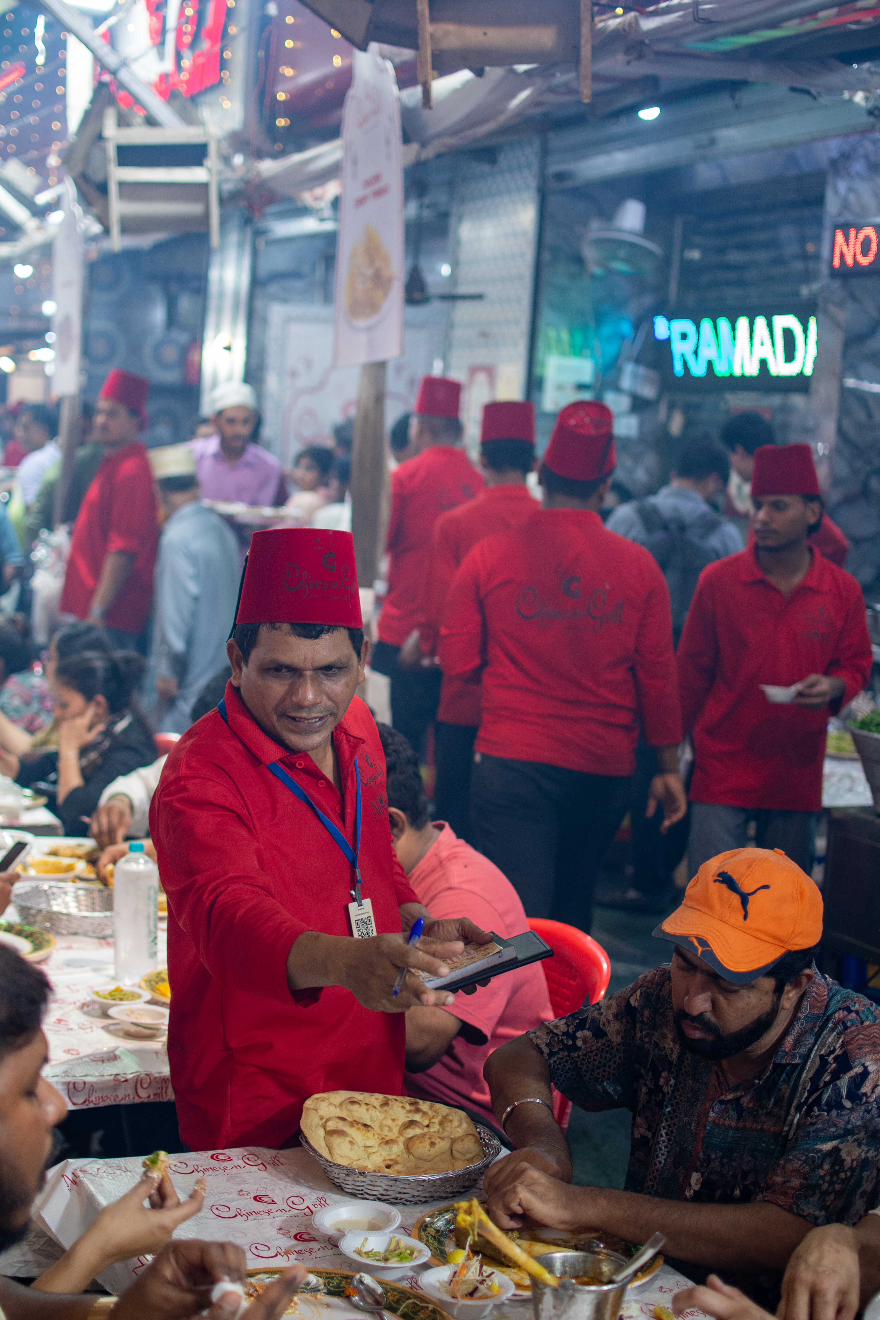 Waiter in red fez serving diners, RAMADAN sign glowing in background
