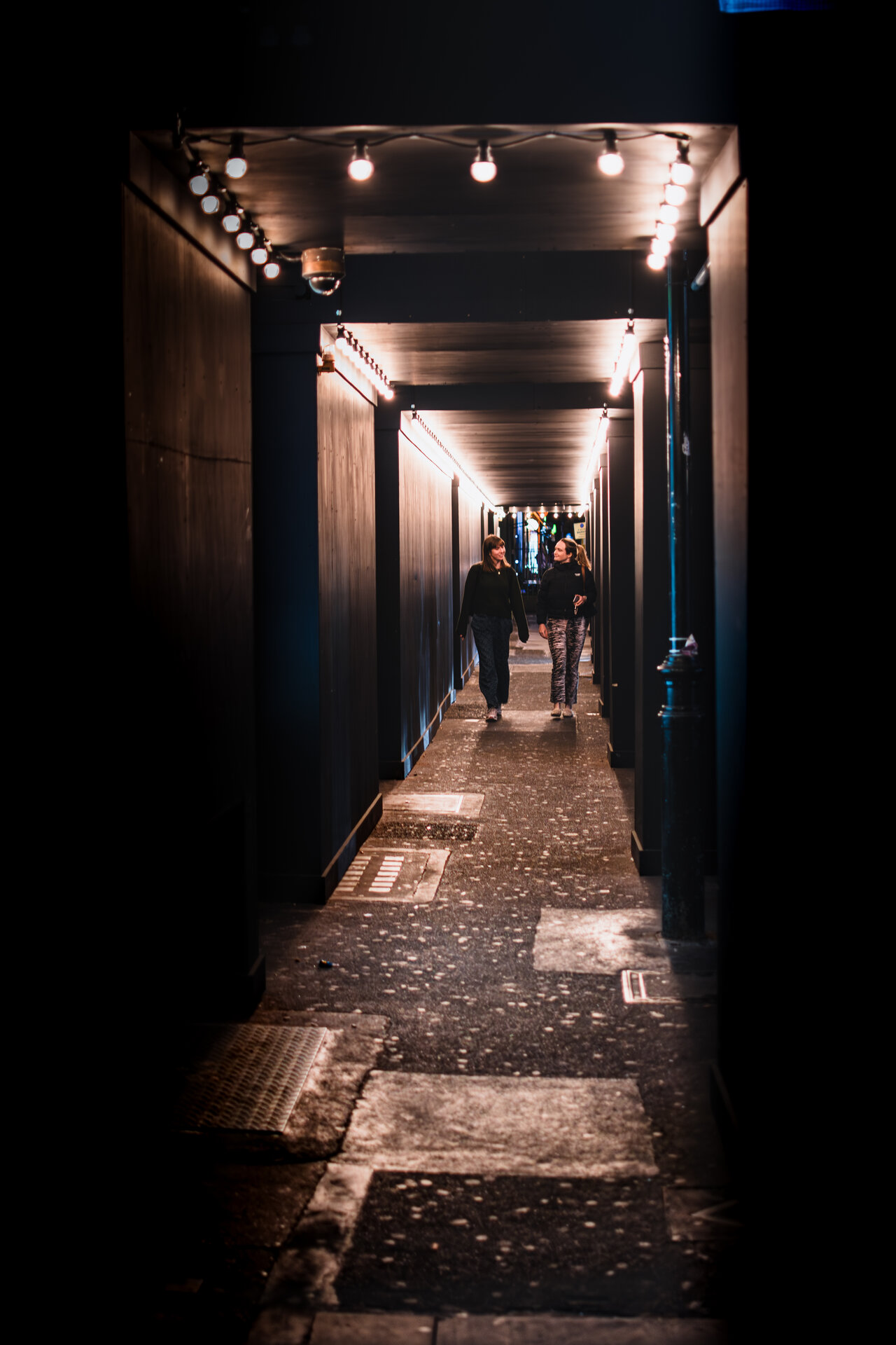 Two women walking and talking through a lit covered passage in Soho at night