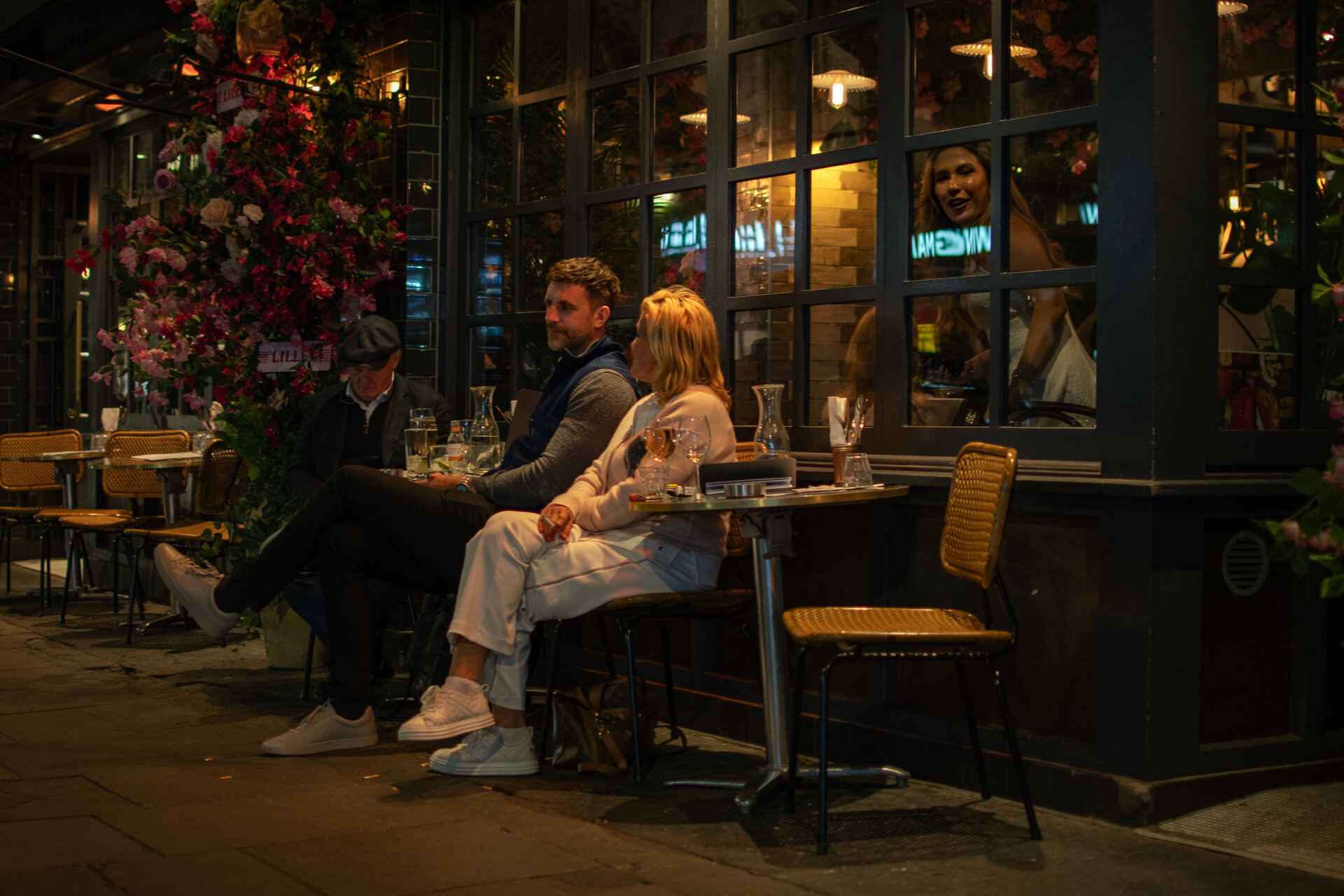 Couple seated outside a cafe at night, woman gazing through the window