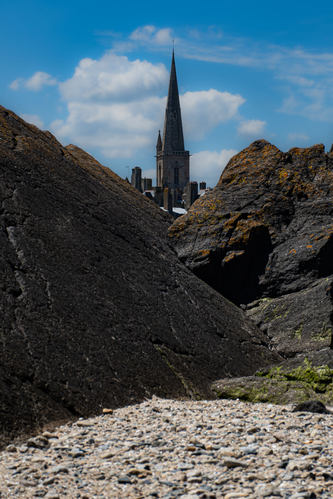 Cathedral spire rising above the walled city, seen through a gap in the tidal rocks