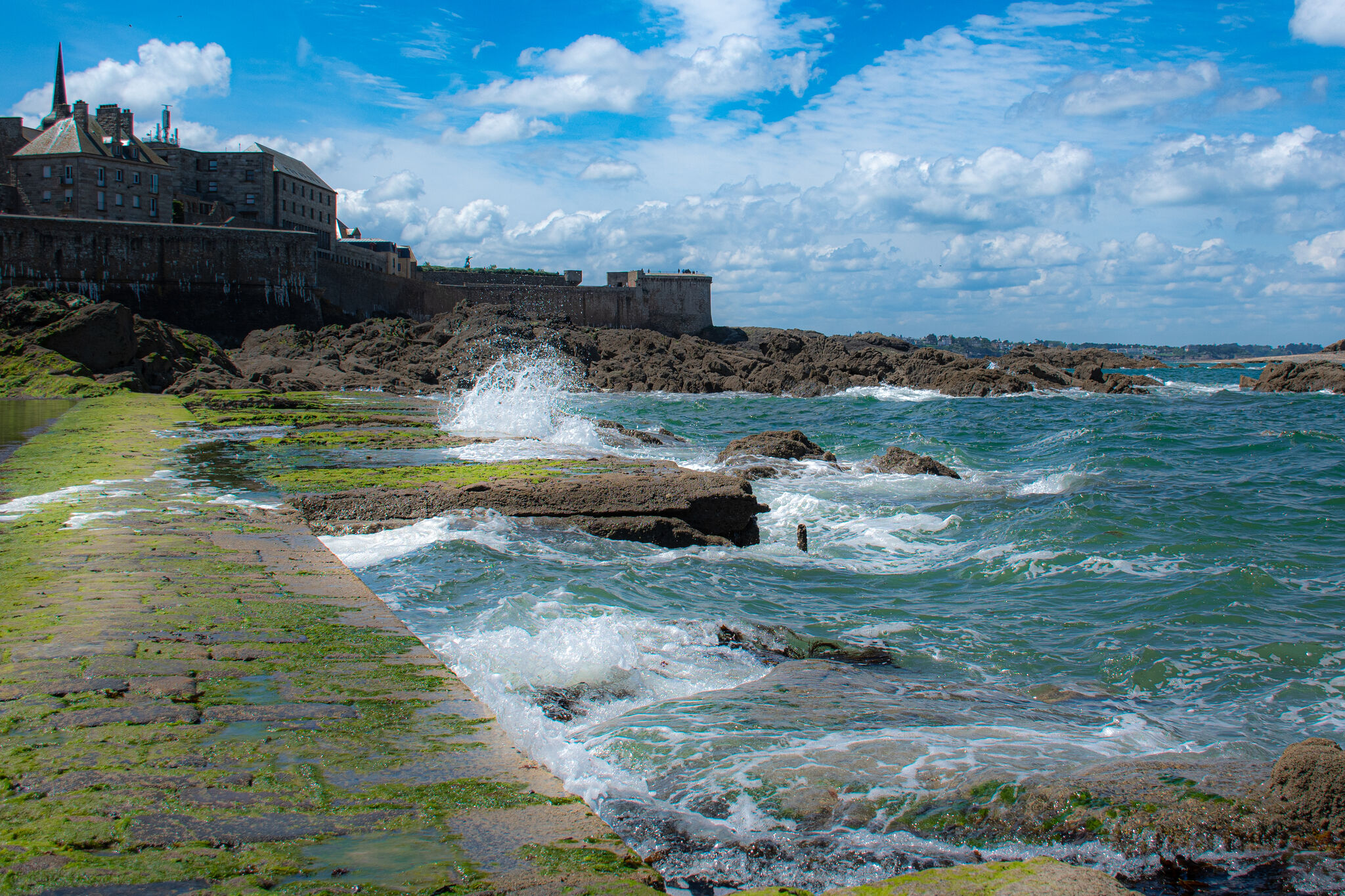 Atlantic waves breaking against a low tidal wall, city ramparts visible in background