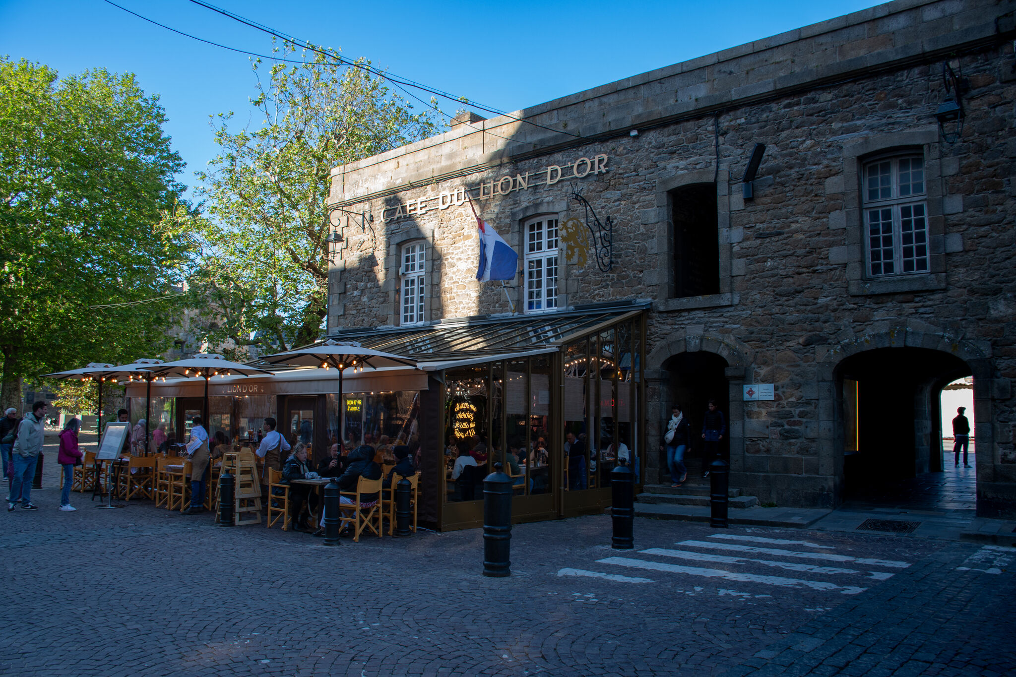 Café du Lion d'Or with people at outdoor tables in the Place Chateaubriand, French flag flying