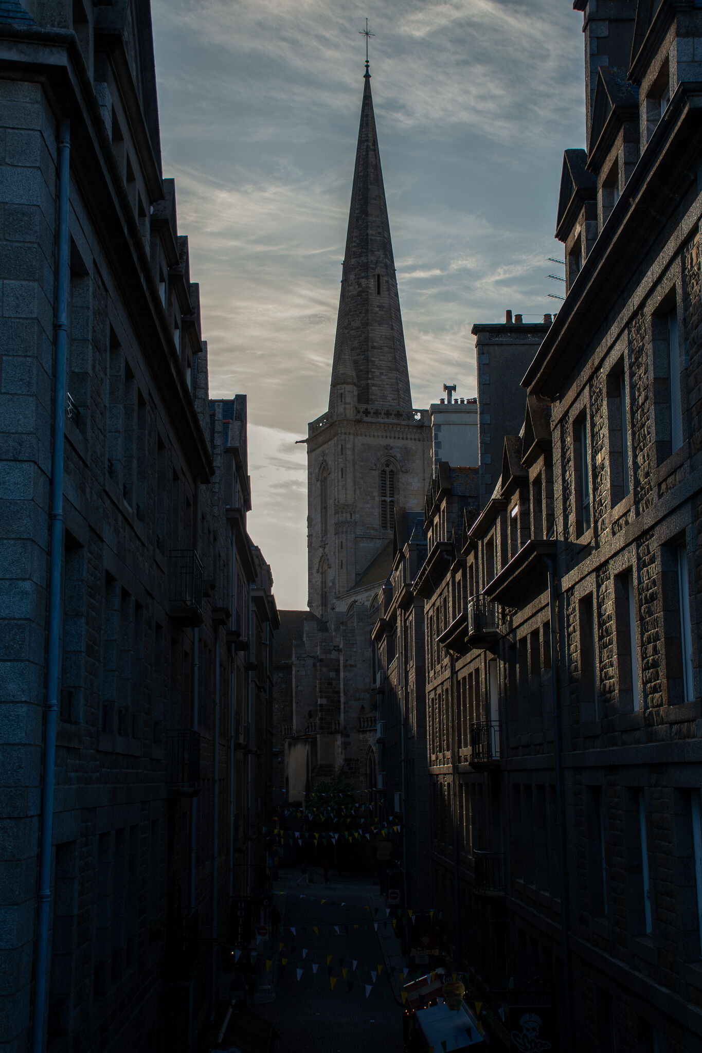 Cathedral spire rising above the narrow streets at blue hour, city in silhouette
